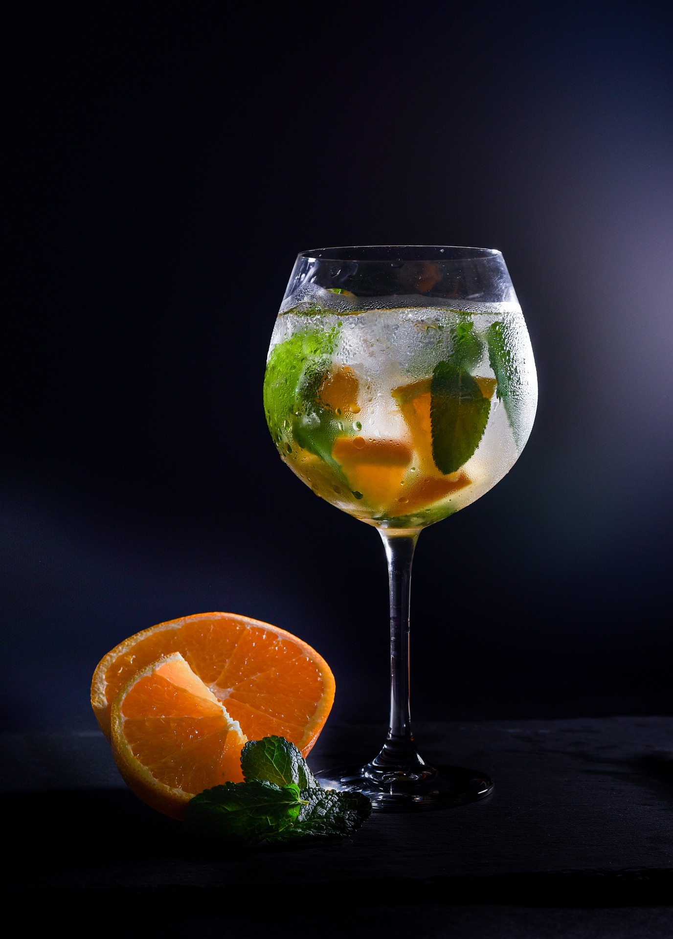 sklenička s pitím alkoholu doplněna pomerančem a ledem